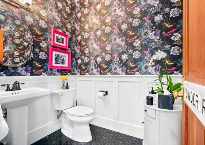 A freshly remodeled bathroom with white, wood-paneled walls topped by colorful wallpaper featuring pink and blue birds and flowers.